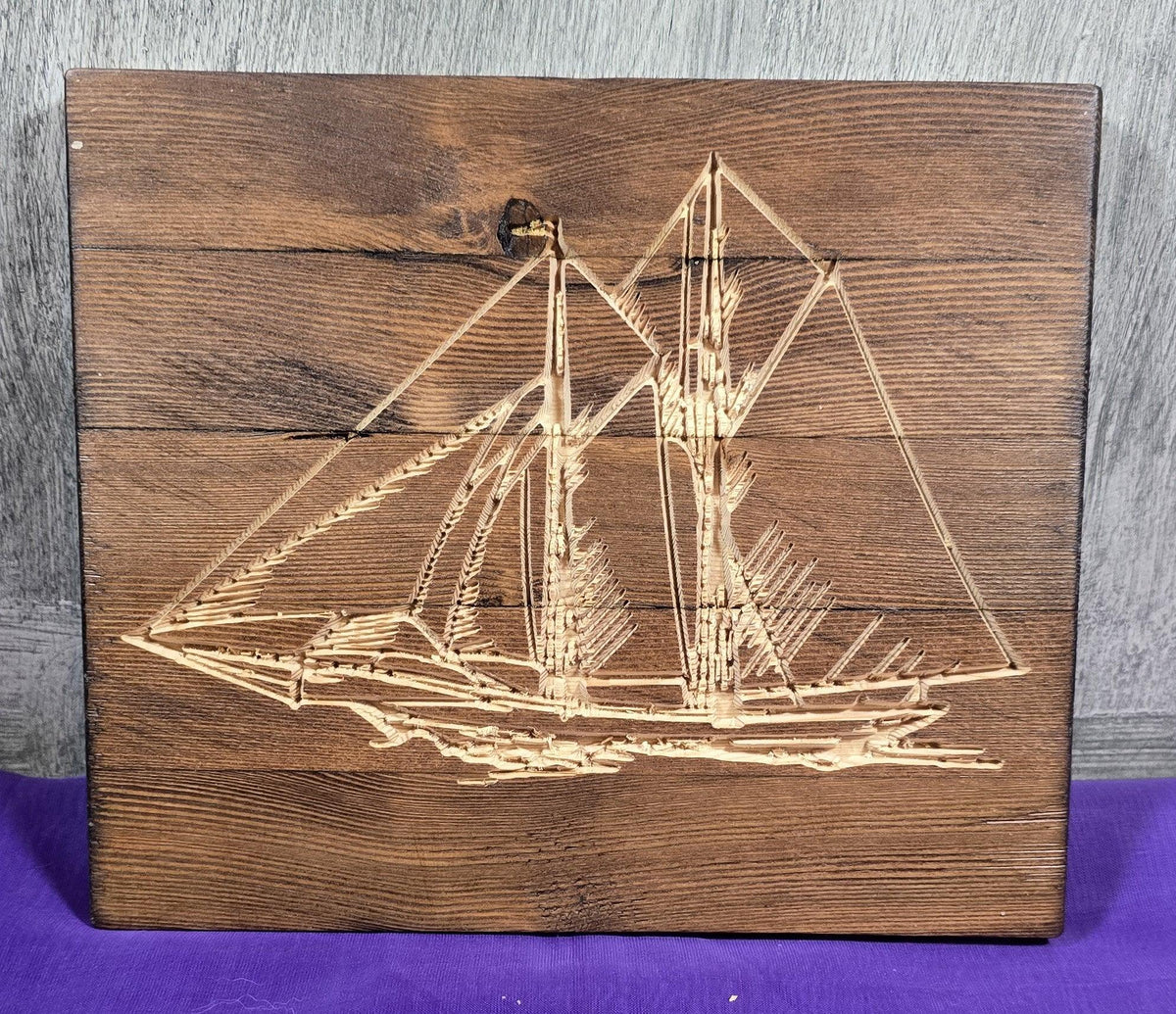 Wooden sailboat carving on a dark wood plaque with detailed sails and hull design.