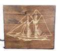 Sailboat engraving on a wooden plaque with detailed rigging and sails, set against a rustic wood background.