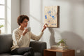 Woman sitting on a sofa touching a TK Wood Designs Aries zodiac wooden wall plaque with blue engraved ram illustration.