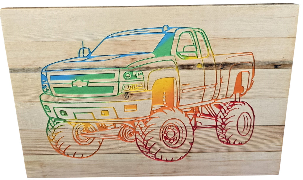 TK Wood Designs rainbow-colored Chevy pickup truck carved into wood. Features large monster truck tires and a rustic wood grain background.