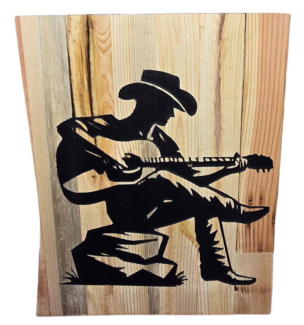 TK Wood Designs reclaimed wood sign featuring a black silhouette of a cowboy playing guitar, seated on a rock.