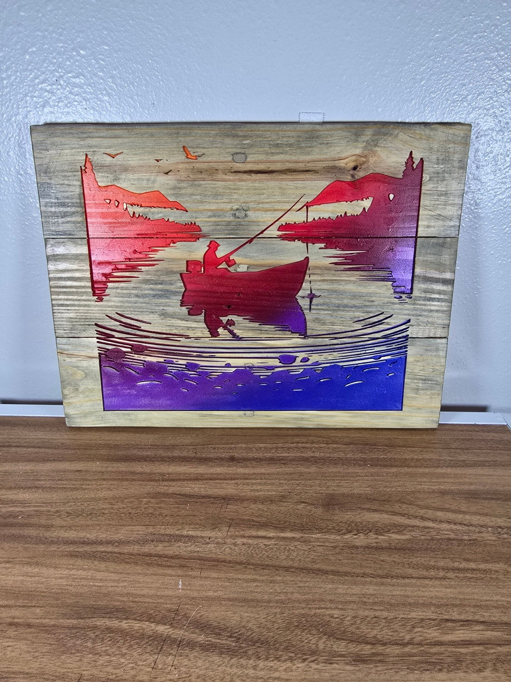 TK Wood Designs rustic wooden wall art featuring a fisherman in a boat with a vibrant red, orange, and purple sunset.