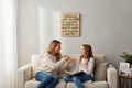 TK Wood Designs natural wood sign with carved text about children's eye-rolling and talking back. A mother and daughter laugh on a couch.