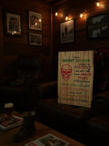 TK Wood Designs rustic wooden wall sign with red skull graphic and humorous text displayed on a leather armchair