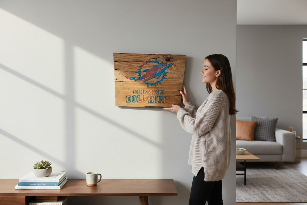 Woman hanging a TK Wood Designs handcrafted wooden Miami Dolphins wall sign with aqua and orange logo in a living room.