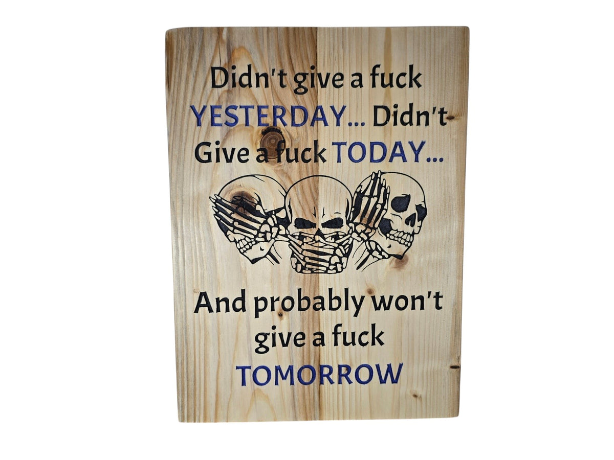 TK Wood Designs wooden wall sign featuring three skulls and bold text in black and blue on a natural wood grain finish.